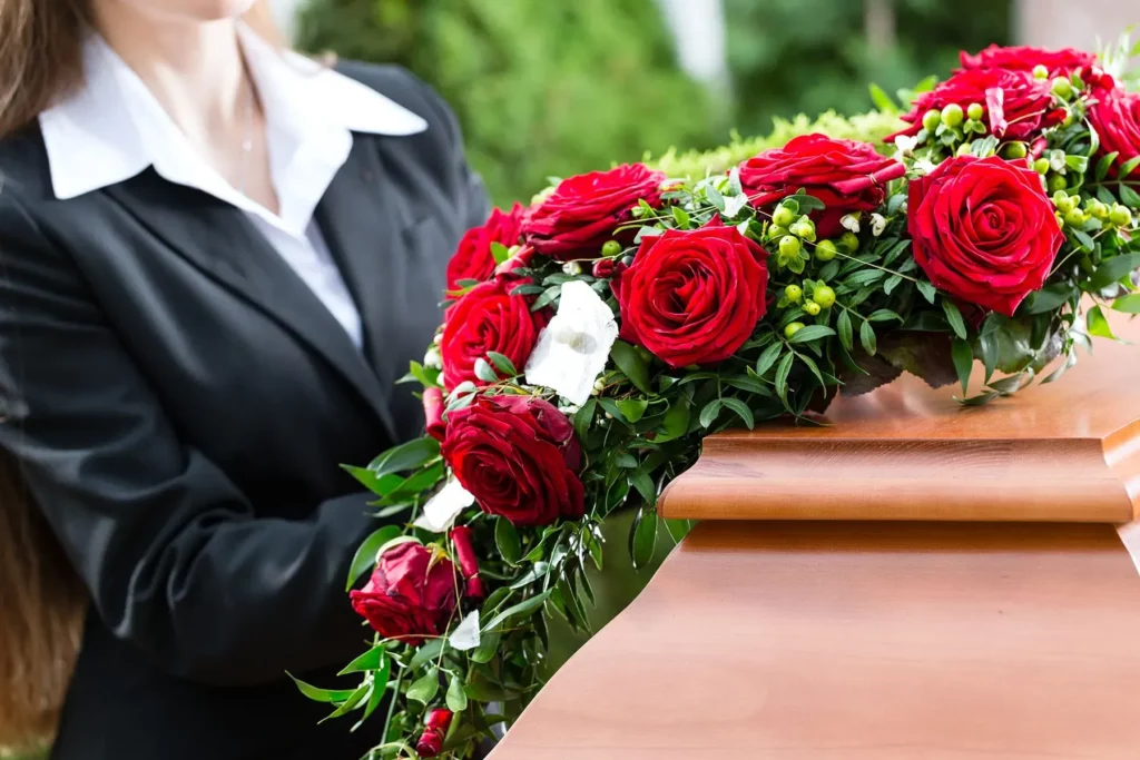 Gerbe de roses rouges et fleurs blanches sur un cercueil en bois verni.