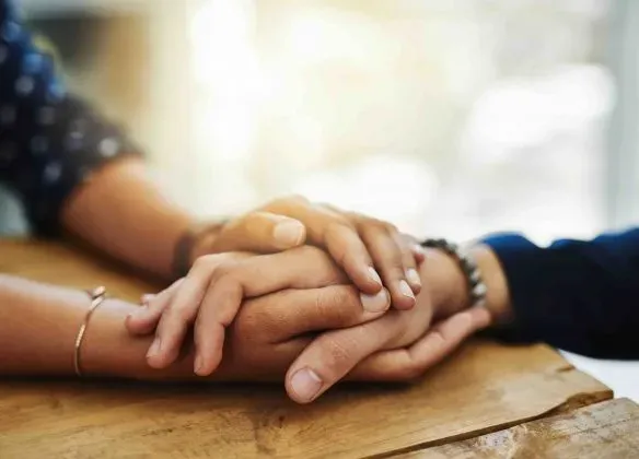 Mains enlacées de deux personnes se tenant sur une table en bois.